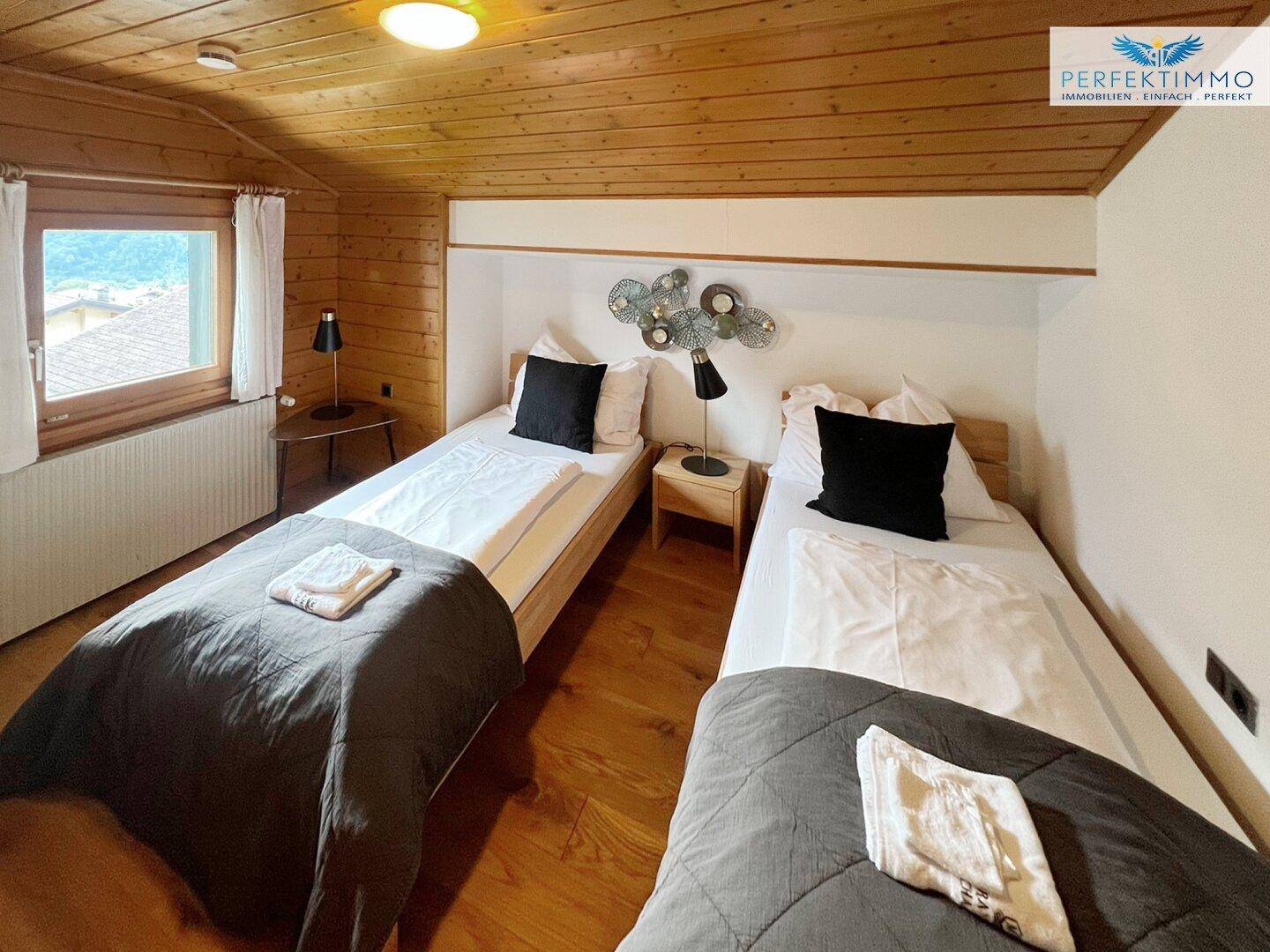 Helles Schlafzimmer mit zwei Einzelbetten, Holzboden und Fenster.