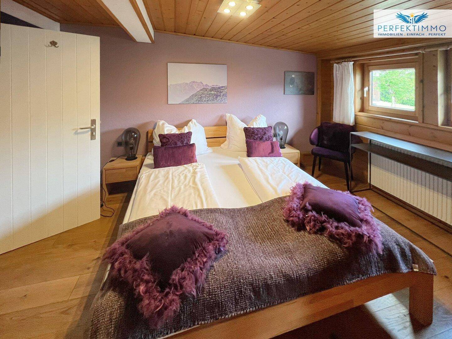 Schlafzimmer mit Doppelbett, Holzboden und lila Kissen.