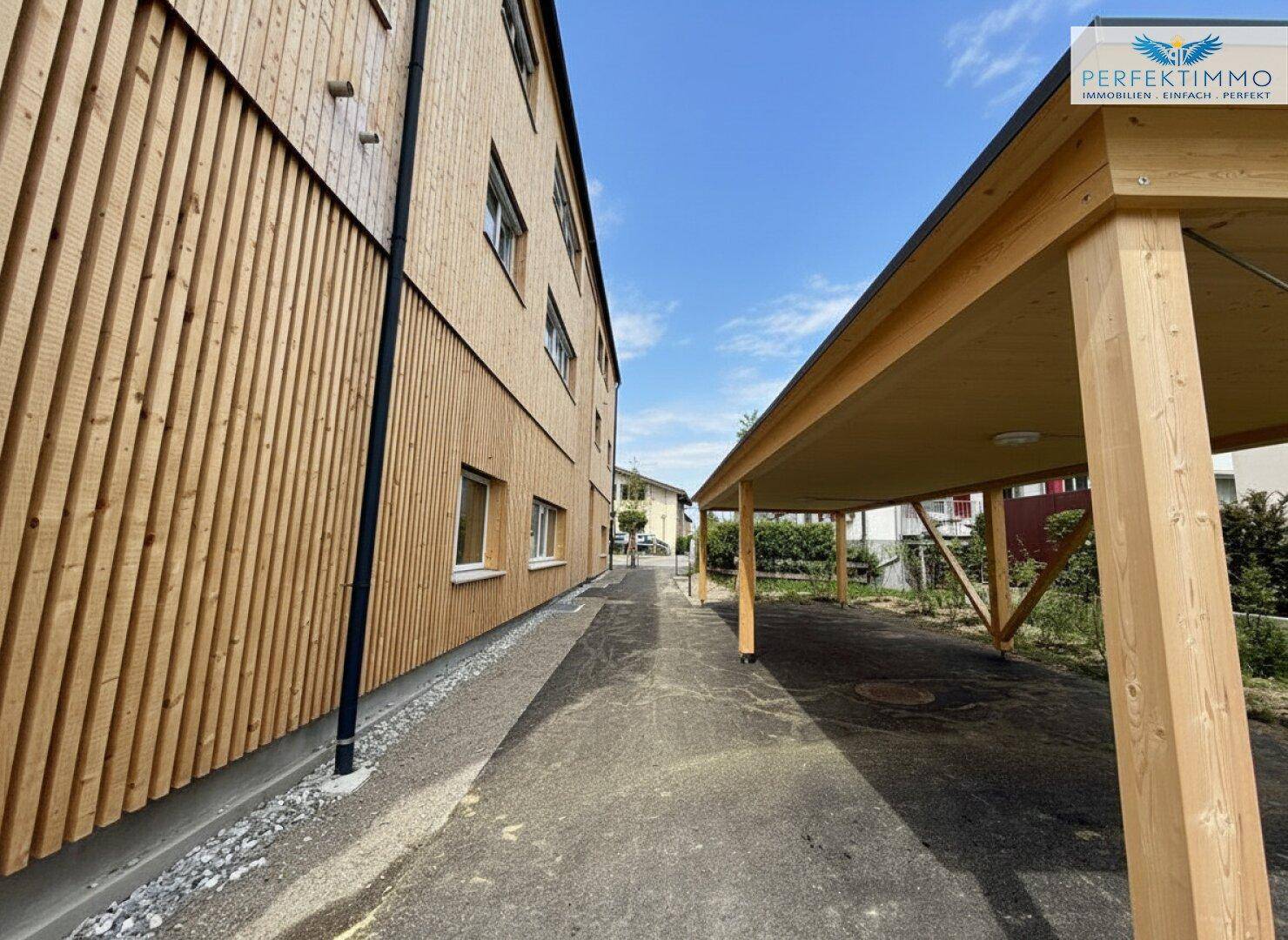 Seitenansicht eines modernen Gebäudes mit Holzfassade und einem angrenzenden Carport.