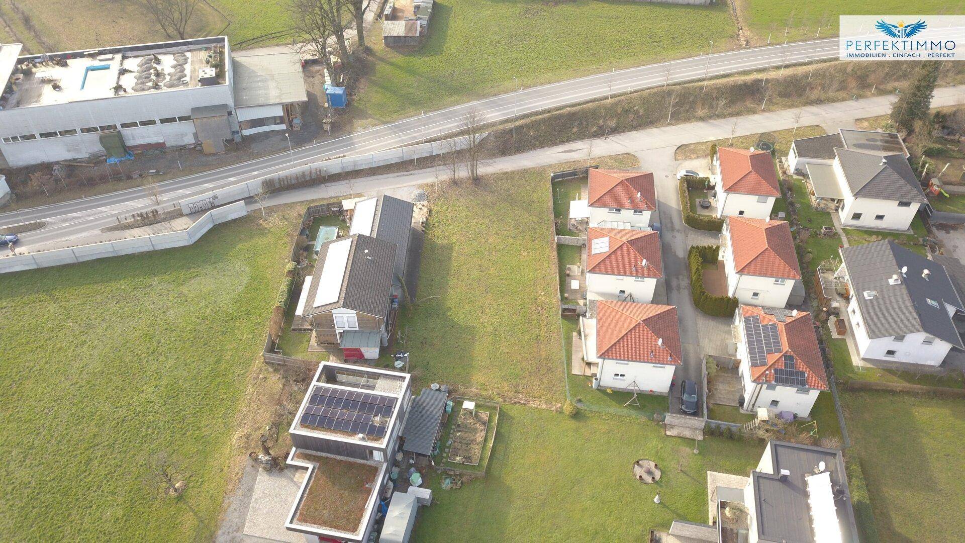 Weitläufige Luftaufnahme einer Wohnsiedlung mit grünen Feldern und einer Landstraße.