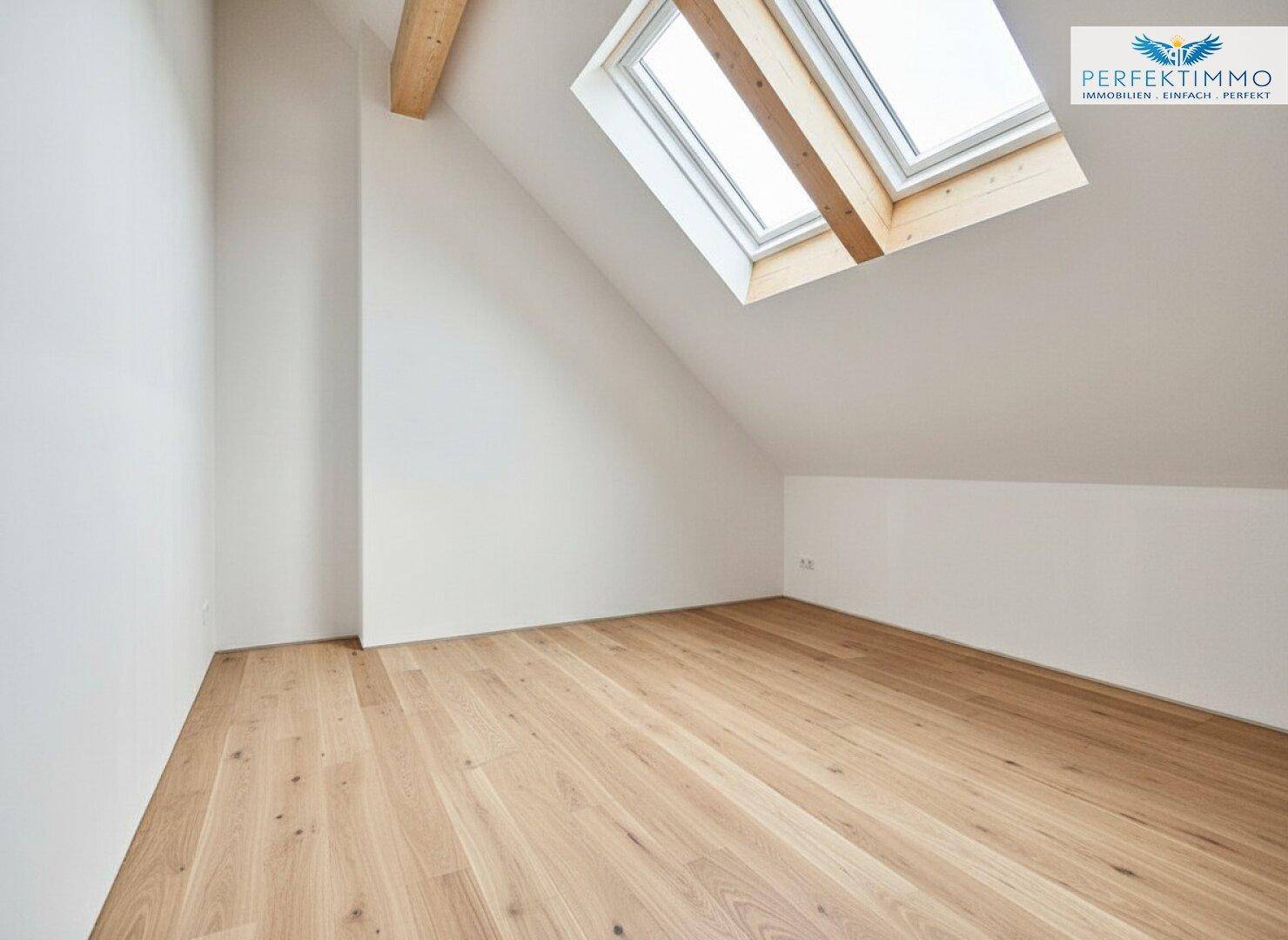 Heller Dachraum mit Holzboden, zwei Dachfenstern und sichtbaren Holzbalken unter der Schräge.