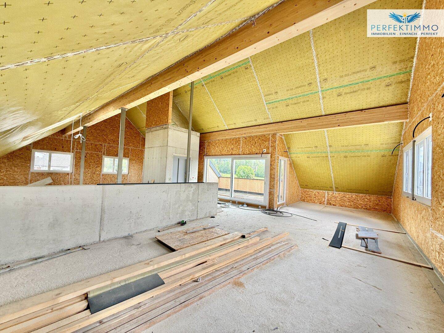 Unfertiger Innenraum im Dachgeschoss mit sichtbaren Holzbalken und Isolierung, bereit für den Ausbau.