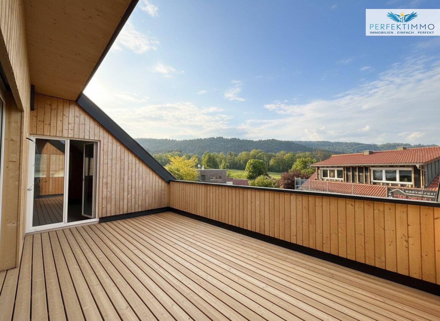 Helle Holzterrasse mit Zugang zum Innenbereich und weitem Blick auf die grüne Umgebung.