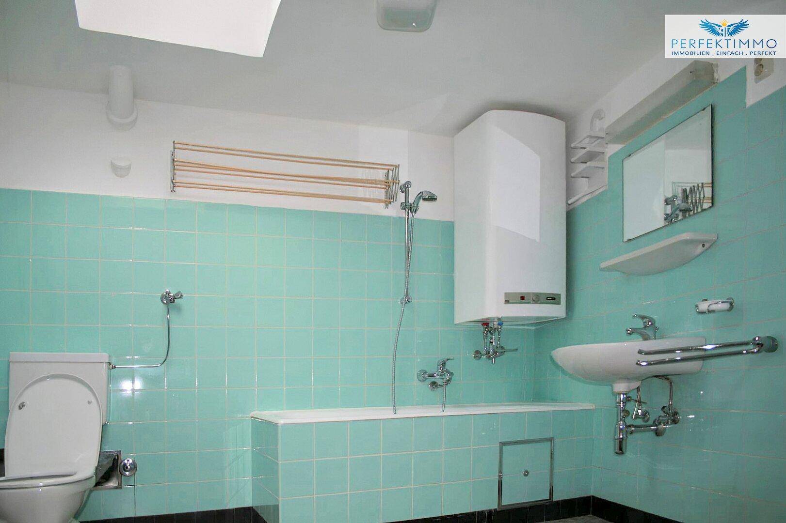 Badezimmer mit türkisfarbenen Fliesen, Toilette, Waschbecken und Duschbereich.