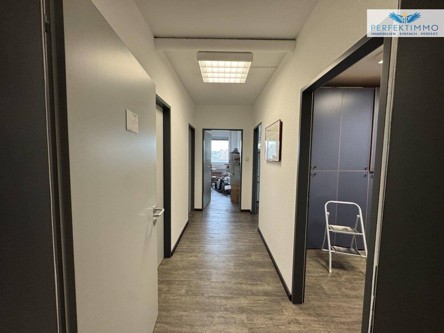 Langer Flur mit mehreren Türen zu Büroräumen, ausgestattet mit modernem Laminatboden und Deckenleuchten.