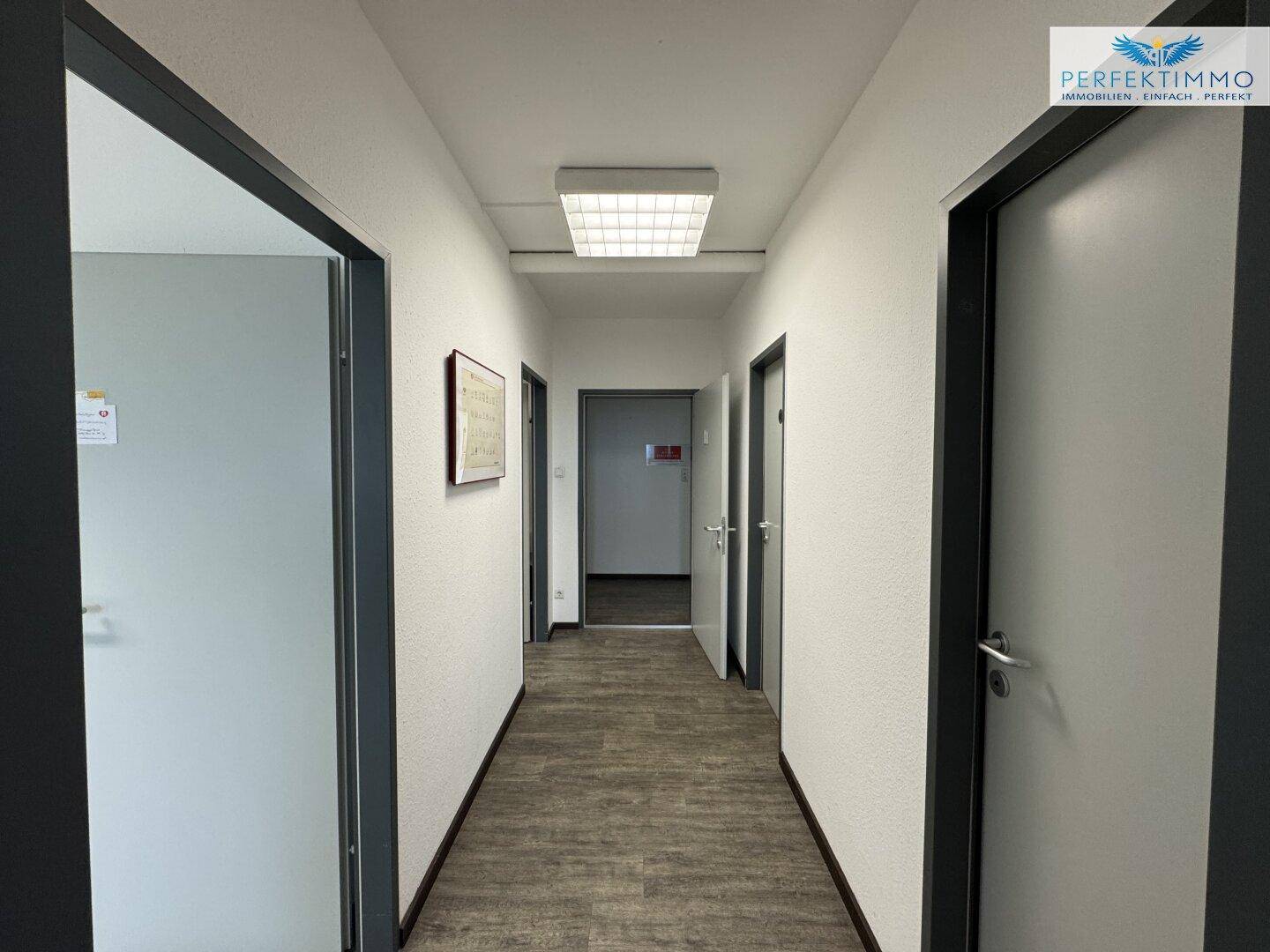 Heller Flur mit Türen zu verschiedenen Räumen, ausgestattet mit Laminatboden und Deckenbeleuchtung.