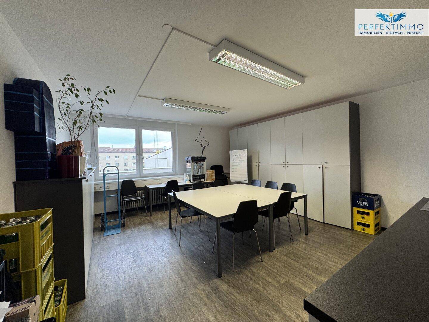 Großes Büro mit Konferenztisch, Schränken und Fenstern, die viel Tageslicht hereinlassen.