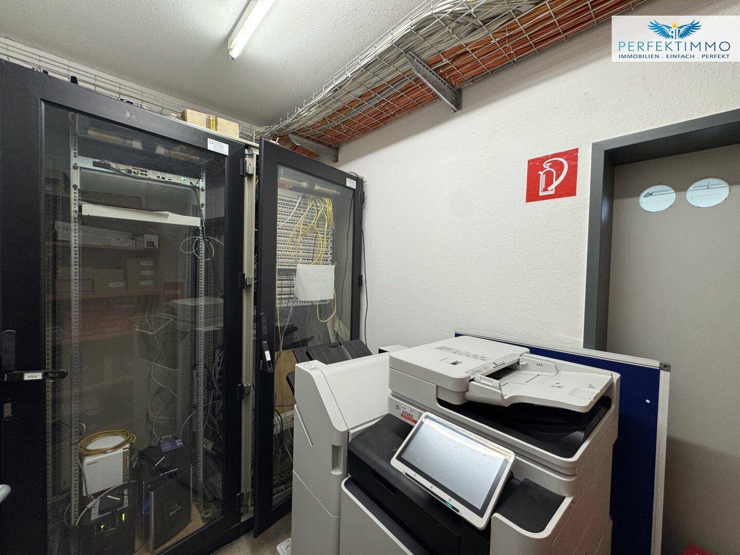 Serverraum mit mehreren Racks, Verkabelung und einem Multifunktionsdrucker, funktional eingerichtet.