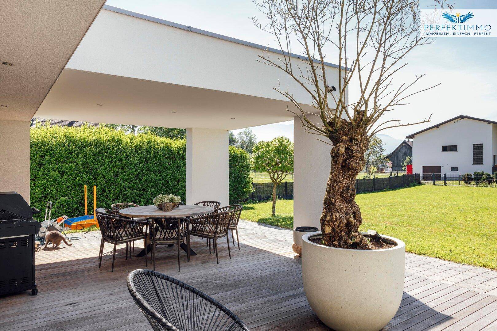 Überdachte Holzterrasse mit Esstisch, Stühlen und einem großen Grill, ideal für Mahlzeiten im Freien.