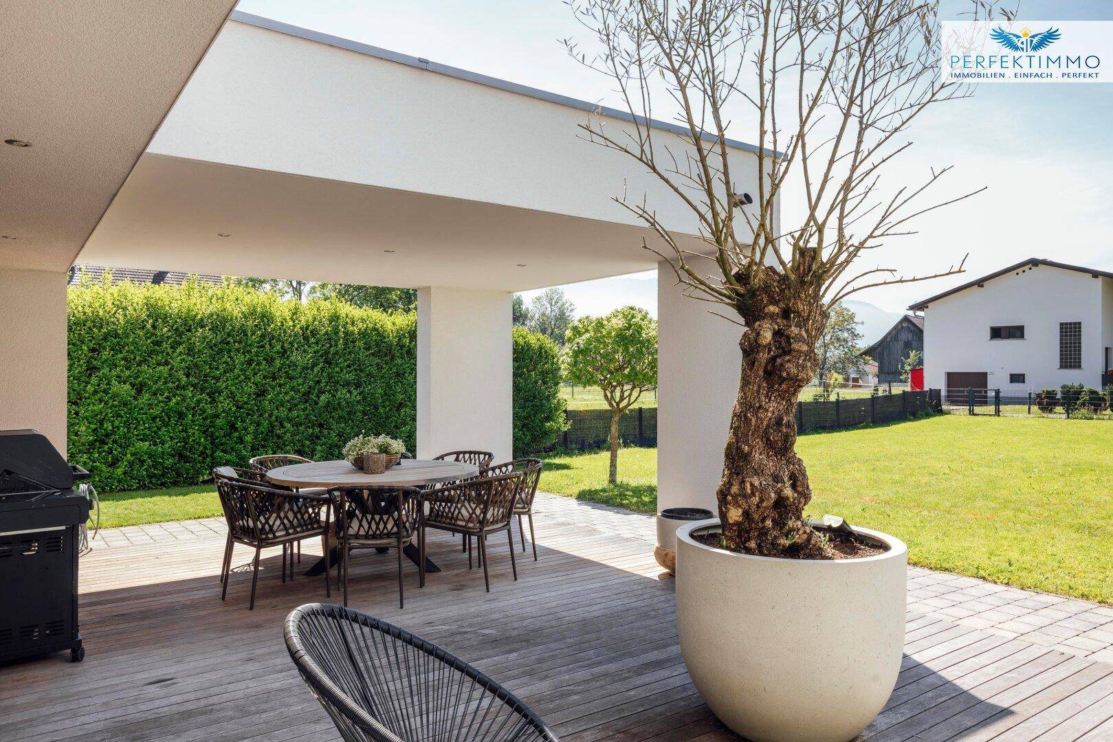 Überdachte Holzterrasse mit Esstisch, Stühlen und einem großen Grill, ideal für Mahlzeiten im Freien.