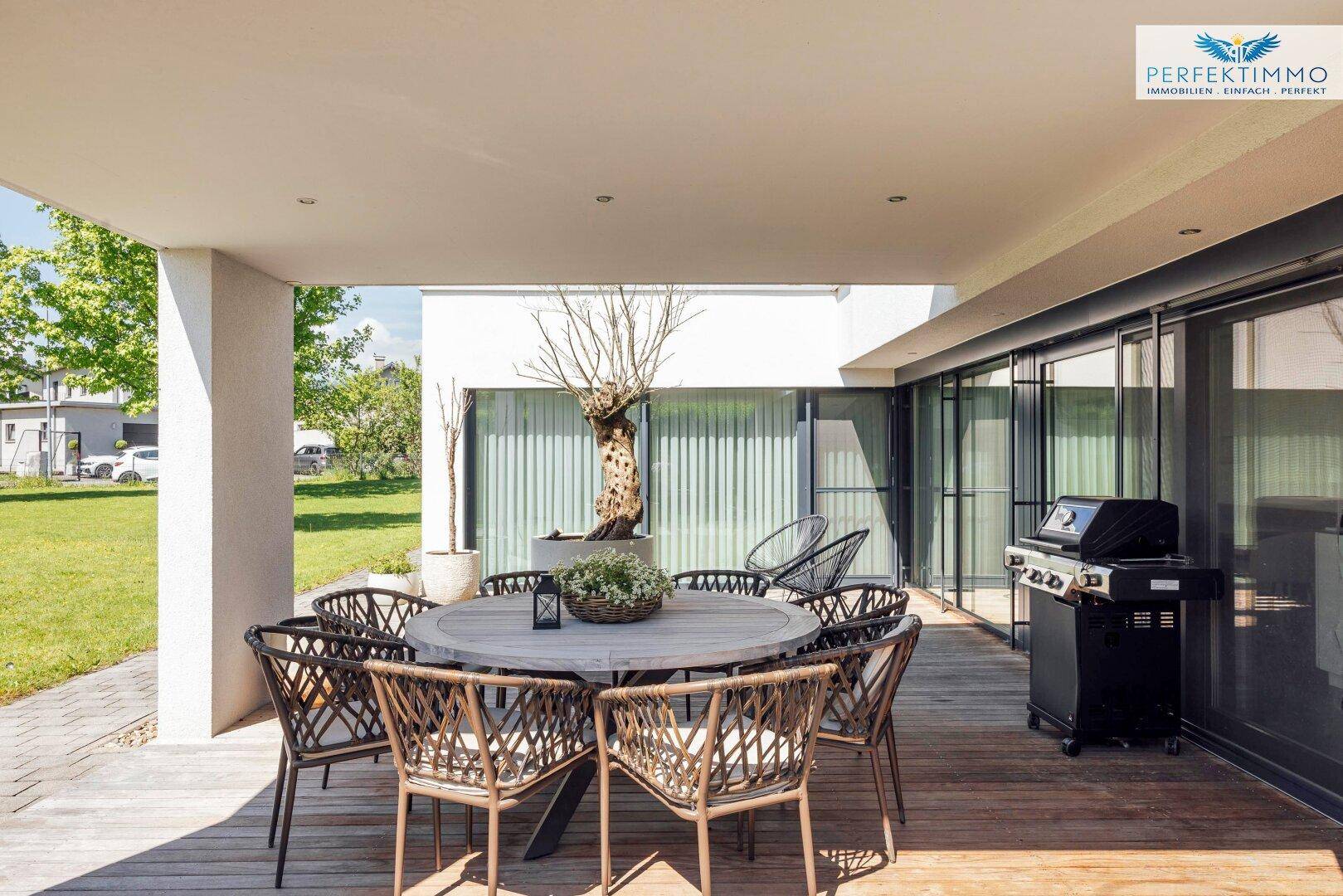 Geräumige überdachte Terrasse mit Essbereich und Grill, direkt zugänglich vom Haus durch große Schiebetüren.