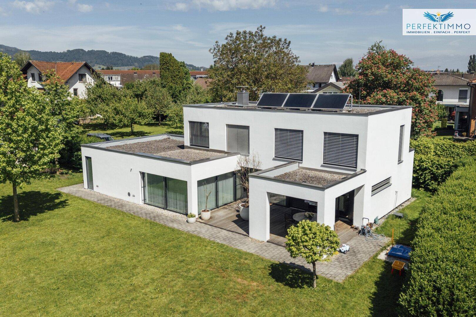 Luftaufnahme des modernen Hauses mit Flachdach, Solaranlage und großem Garten in ländlicher Umgebung.