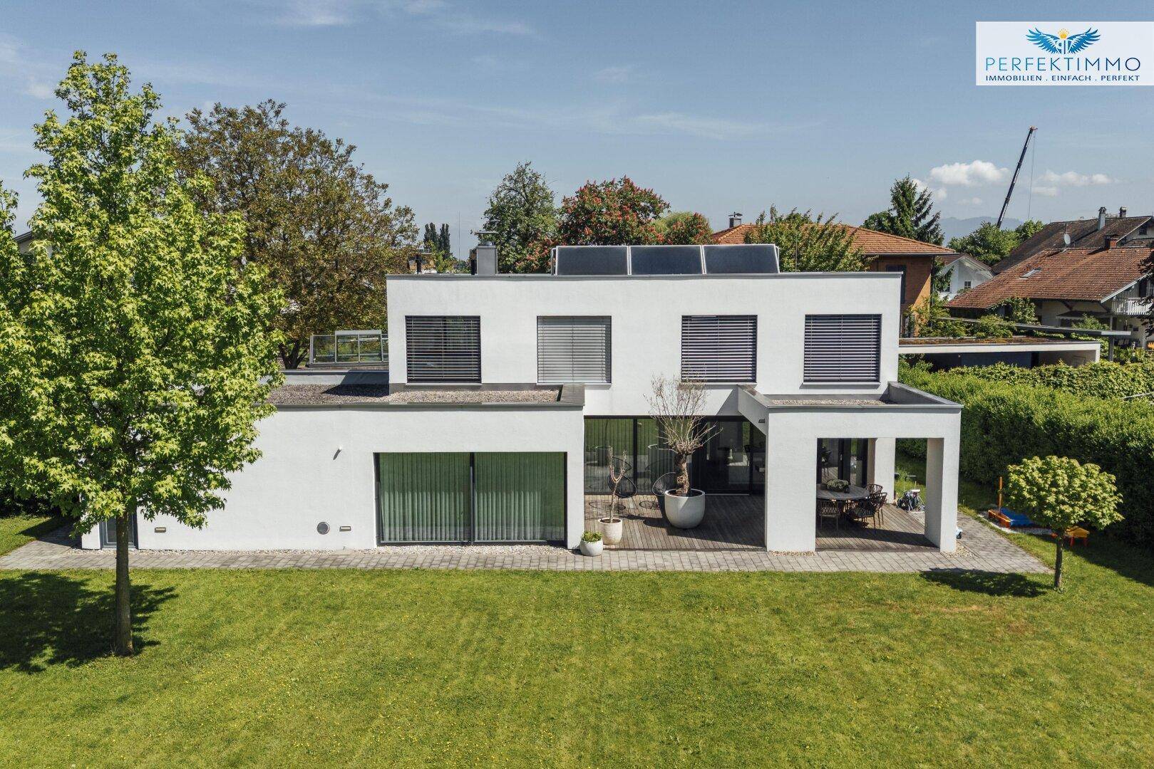 Weitläufige Ansicht des modernen Einfamilienhauses mit Solarpaneelen auf dem Flachdach und weitläufigem Garten.