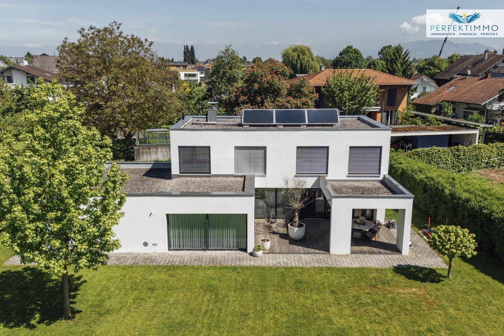 Luftaufnahme des modernen Hauses mit Flachdach, Solaranlage und großem Garten in ländlicher Umgebung.