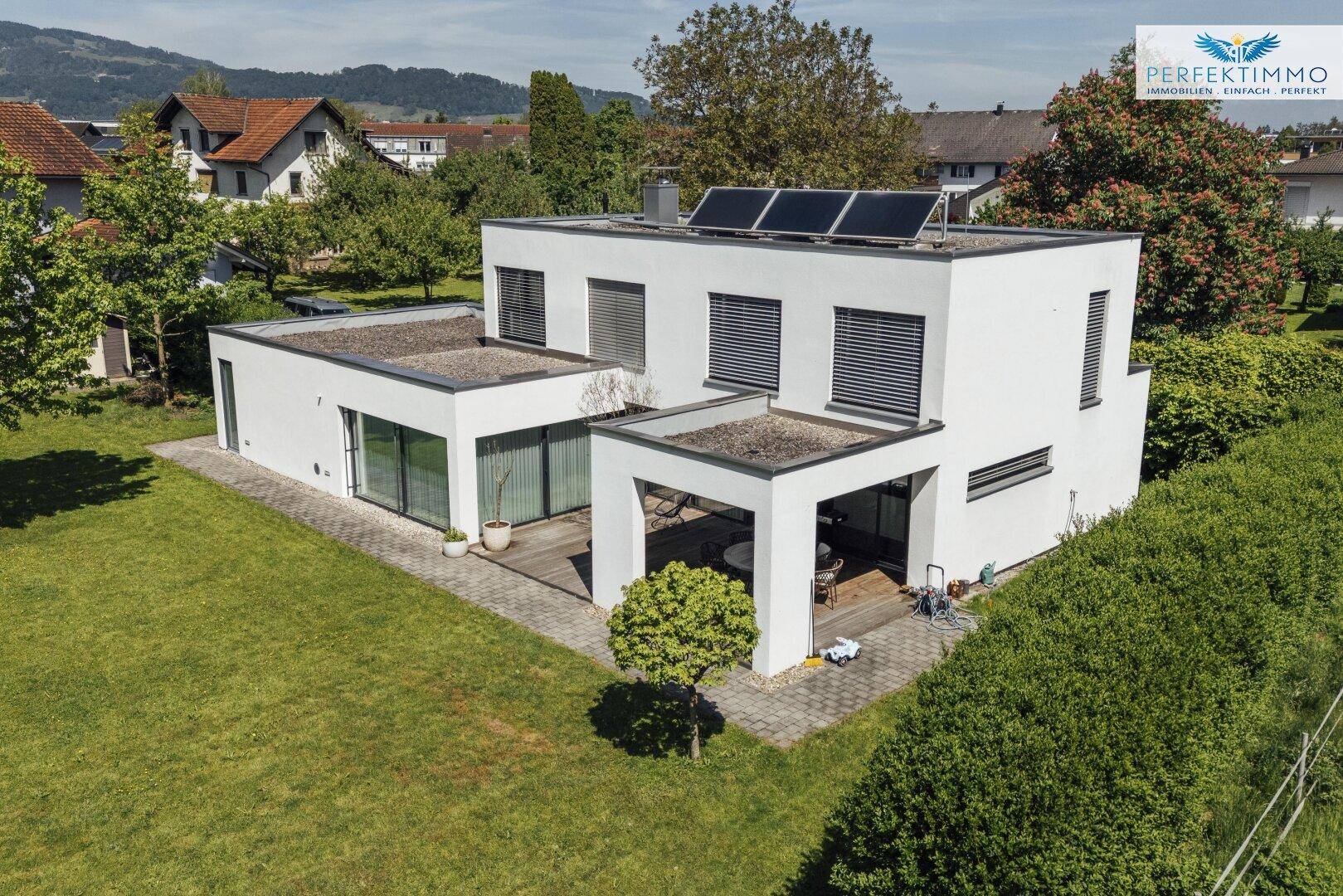 Luftaufnahme des modernen Hauses mit Flachdach, Solaranlage und großem Garten in ländlicher Umgebung.