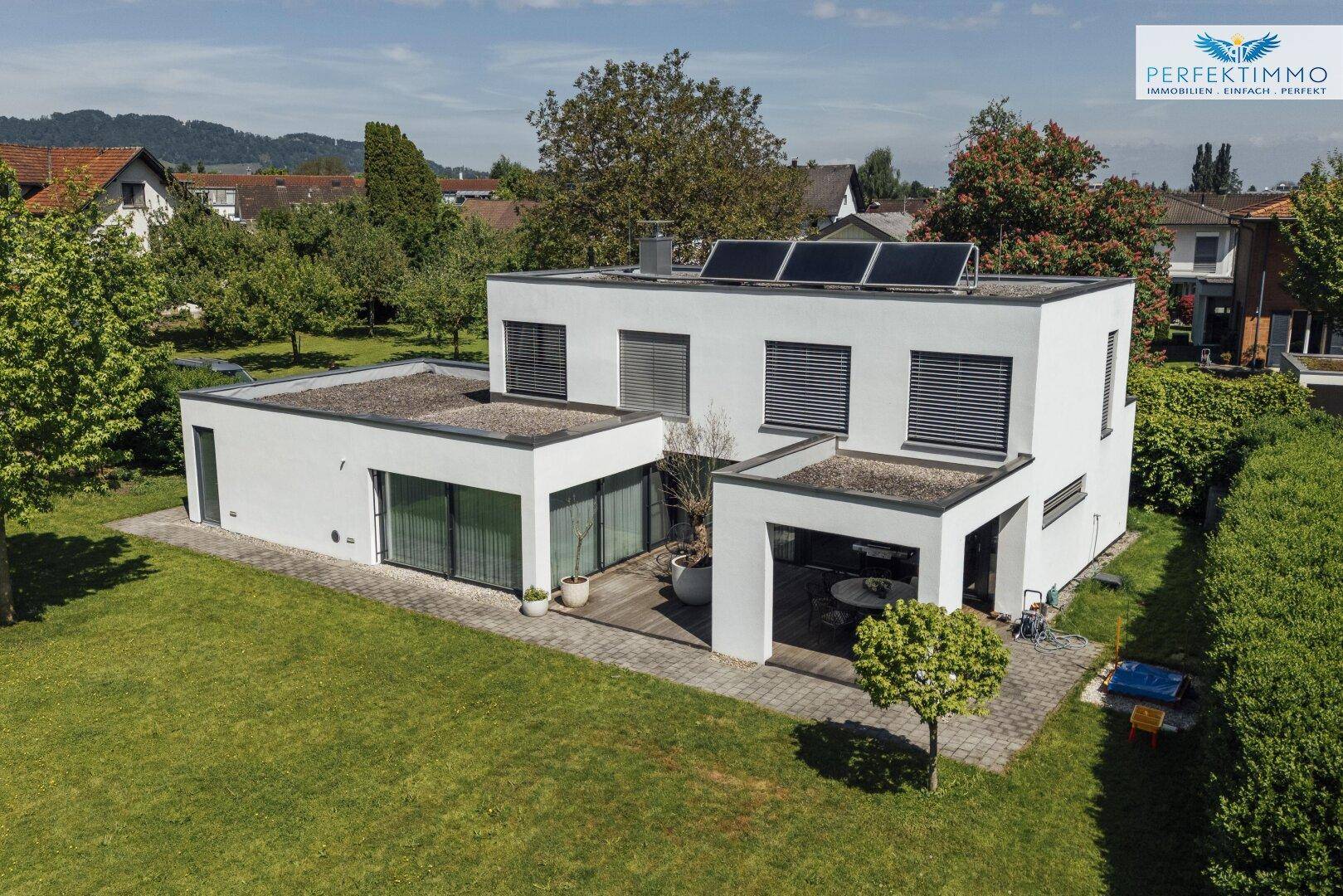 Luftaufnahme des modernen Hauses mit Flachdach, Solaranlage und großem Garten in ländlicher Umgebung.