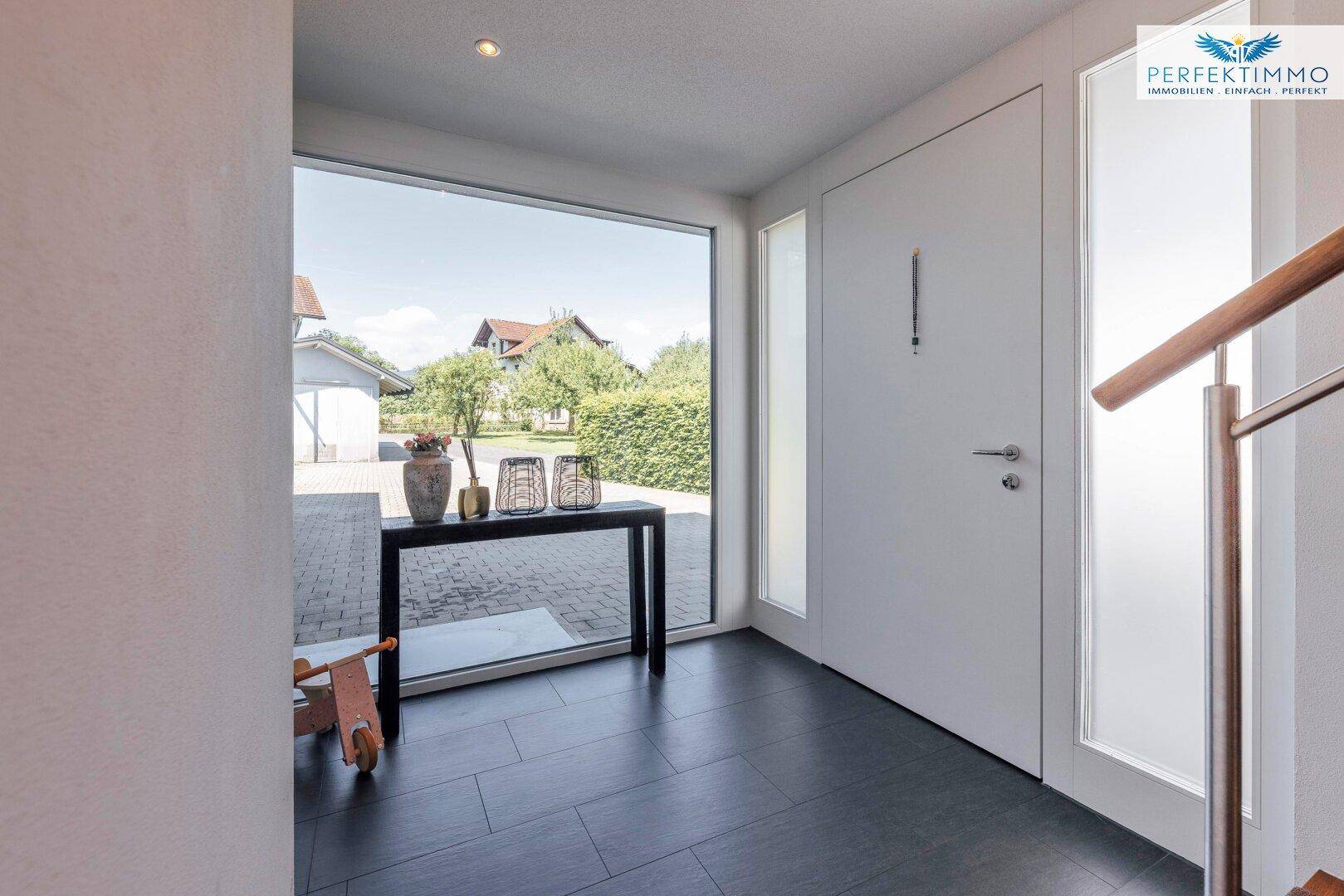 Heller Eingangsbereich mit dunklen Fliesen, moderner Konsole und großem Fenster zur Einfahrt.