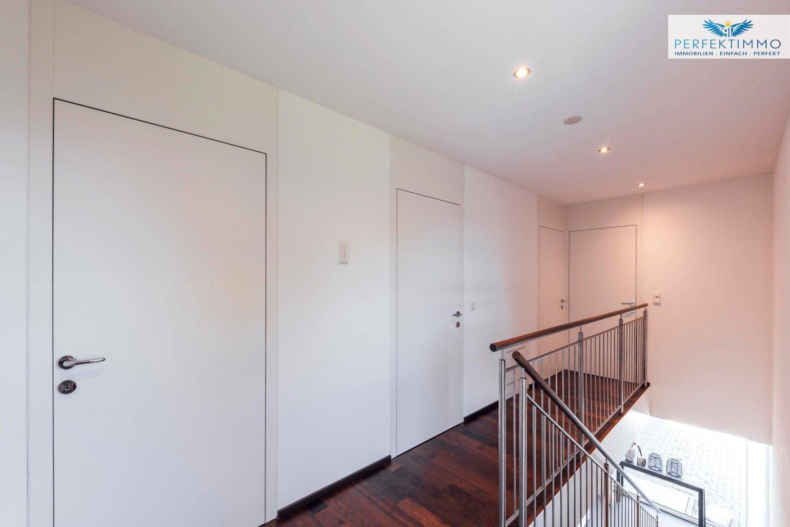 Modernes Treppenhaus mit dunklem Holzboden, schlichten weißen Türen und indirekter Beleuchtung.