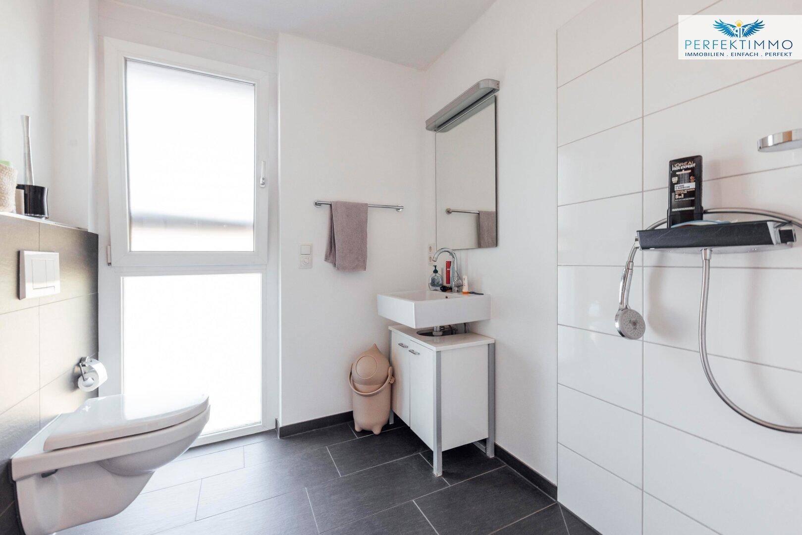 Helles Badezimmer mit moderner Dusche, wandhängendem WC, Einzelwaschbecken und Fenster.