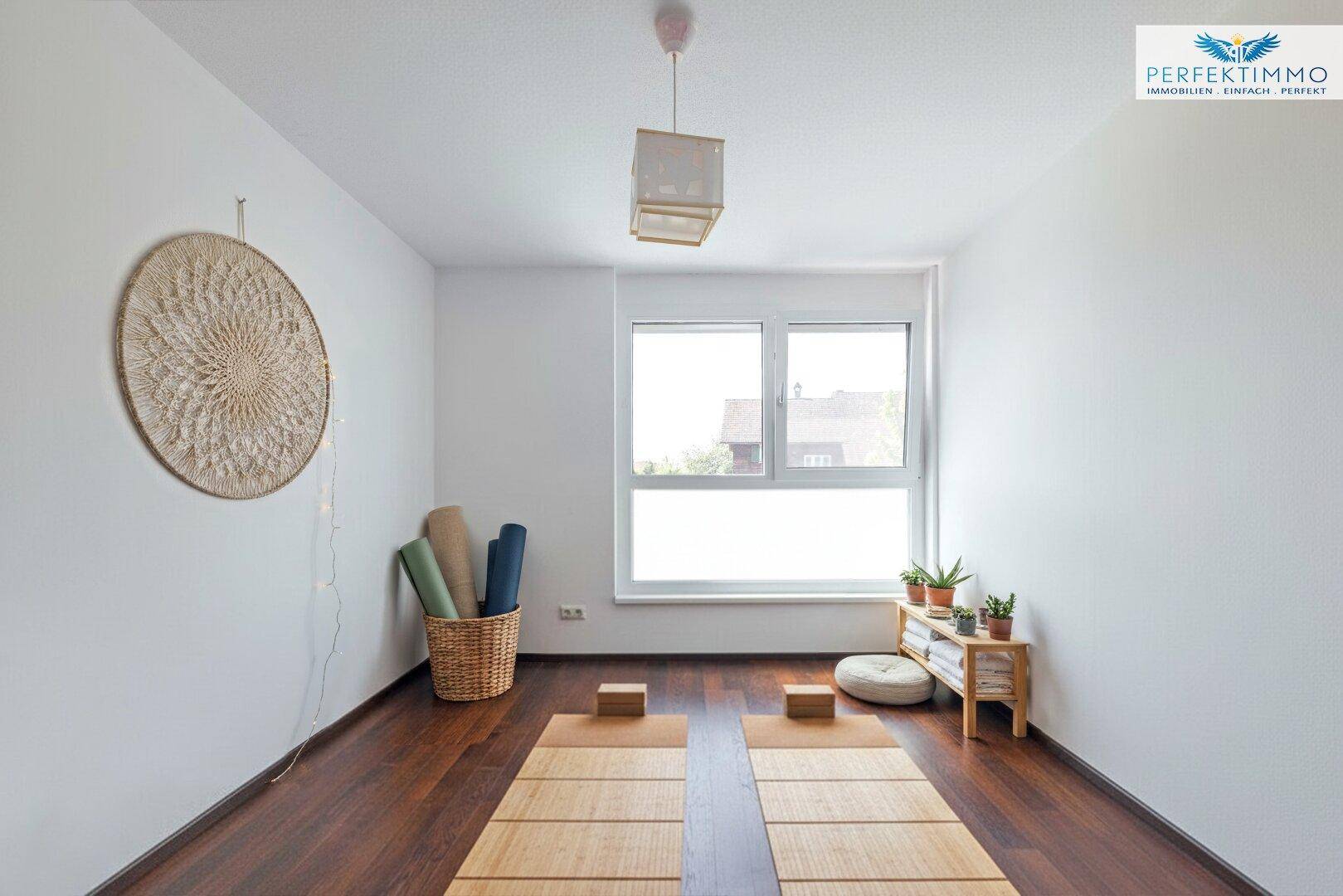Ruhiger Raum mit dunklem Holzboden, großem Fenster und minimalistischer Dekoration, ideal für Yoga.