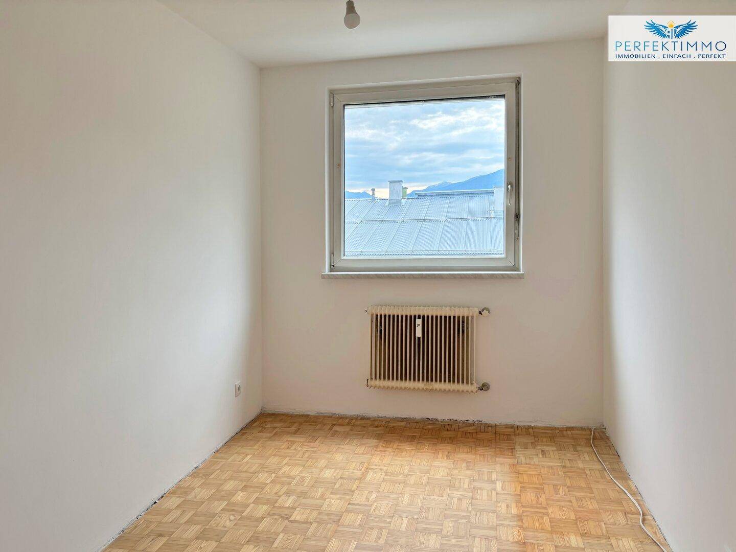 Helles Schlafzimmer mit Parkettboden und einem Fenster, das viel Tageslicht hereinlässt.