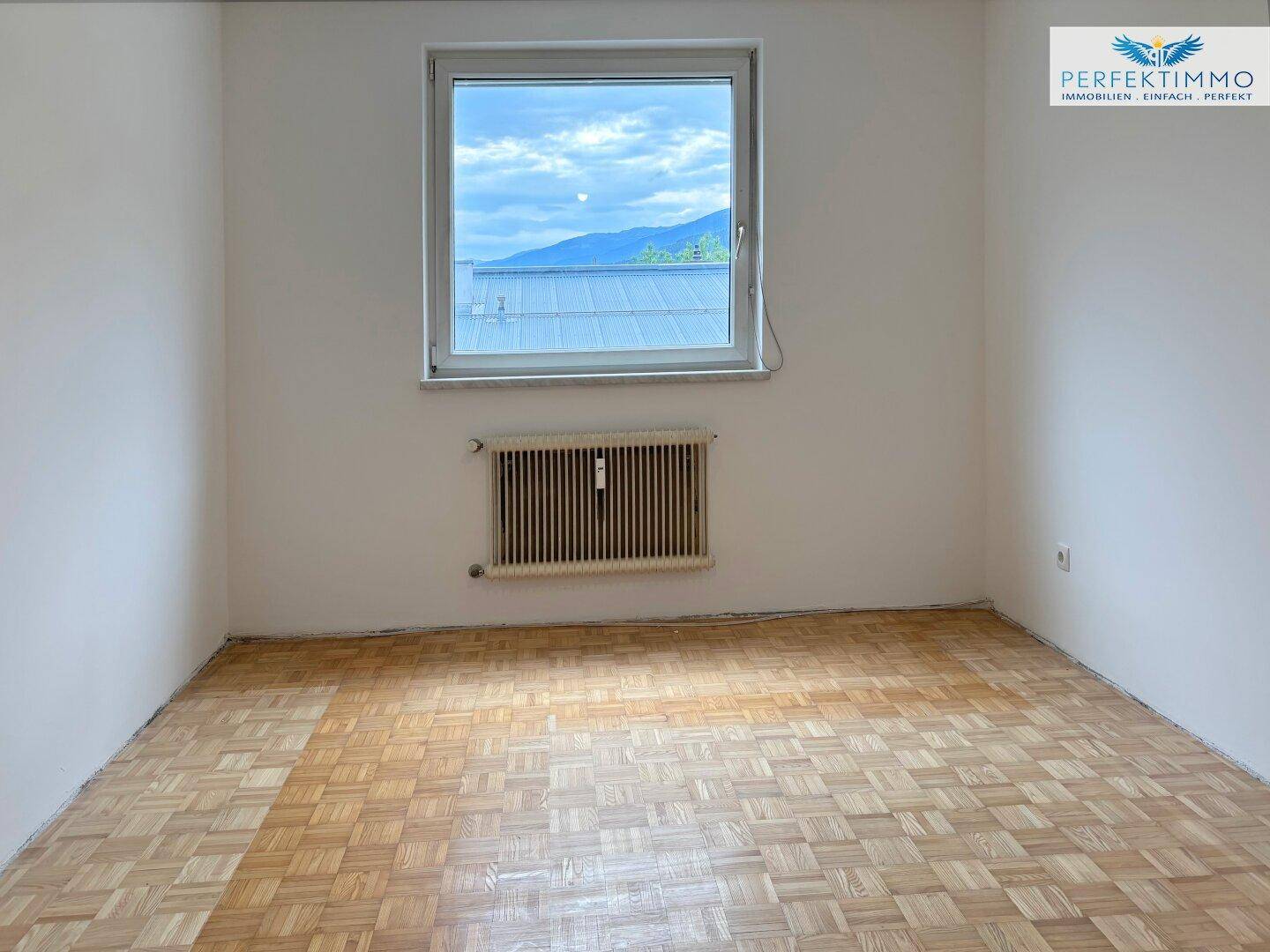 Geräumiges Schlafzimmer mit klassischem Parkettboden und einem großen Fenster für natürliche Belichtung.