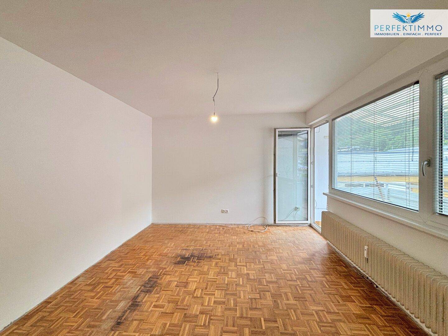 Leeres Wohnzimmer mit Fischgrätparkett und großen Fenstern, bereit zur individuellen Gestaltung und Nutzung.