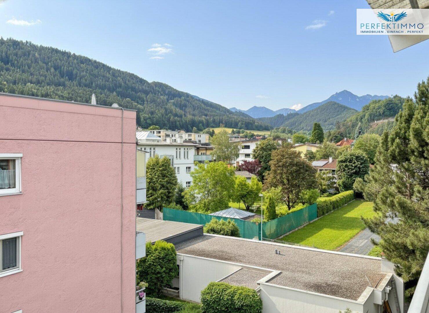 Panoramablick auf die umliegende Wohngegend mit viel Grün und majestätischen Bergen im Hintergrund.