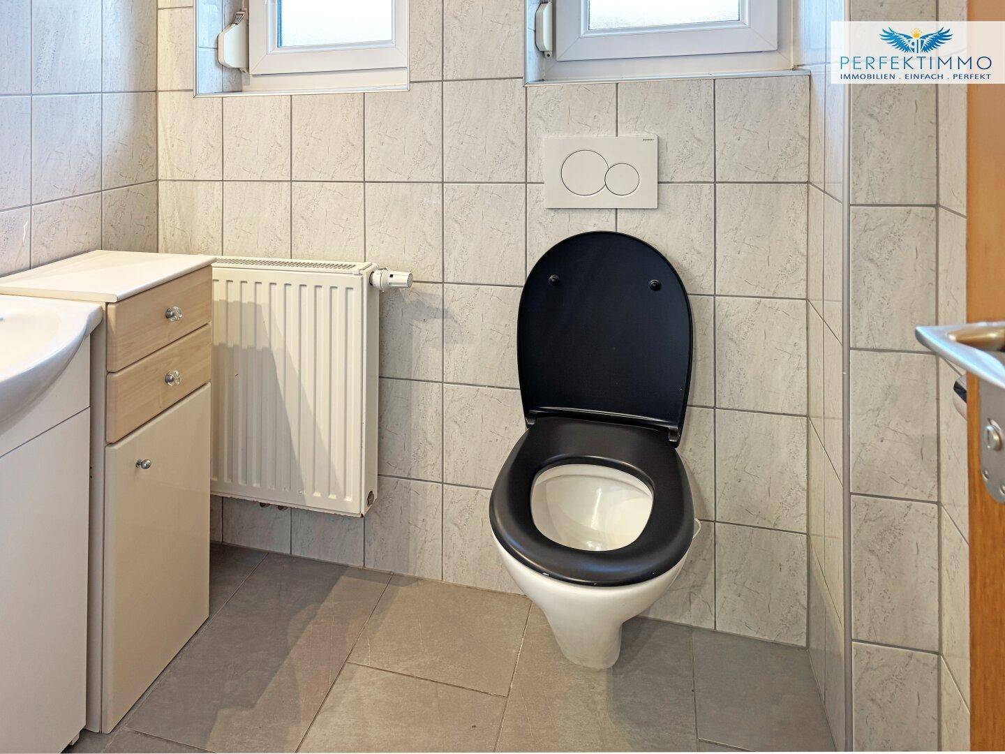 Kleines Gäste-WC mit Wand-WC, Waschbecken und Fliesenboden in neutralen Farben.
