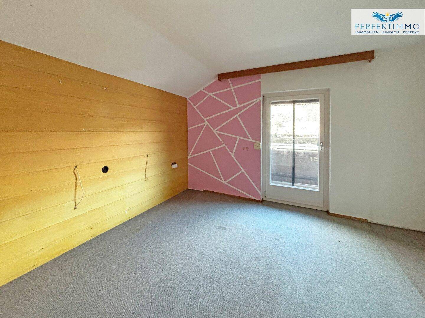 Unfertiges Zimmer mit Holzverkleidung und Zugang zu einem potenziellen Balkon oder Terrasse.