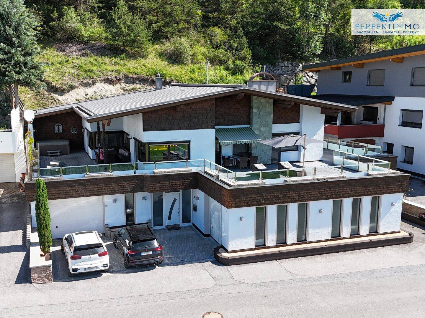 Vorderansicht eines modernen Hauses mit Garagen, Terrassen und einer gepflegten Außenanlage.