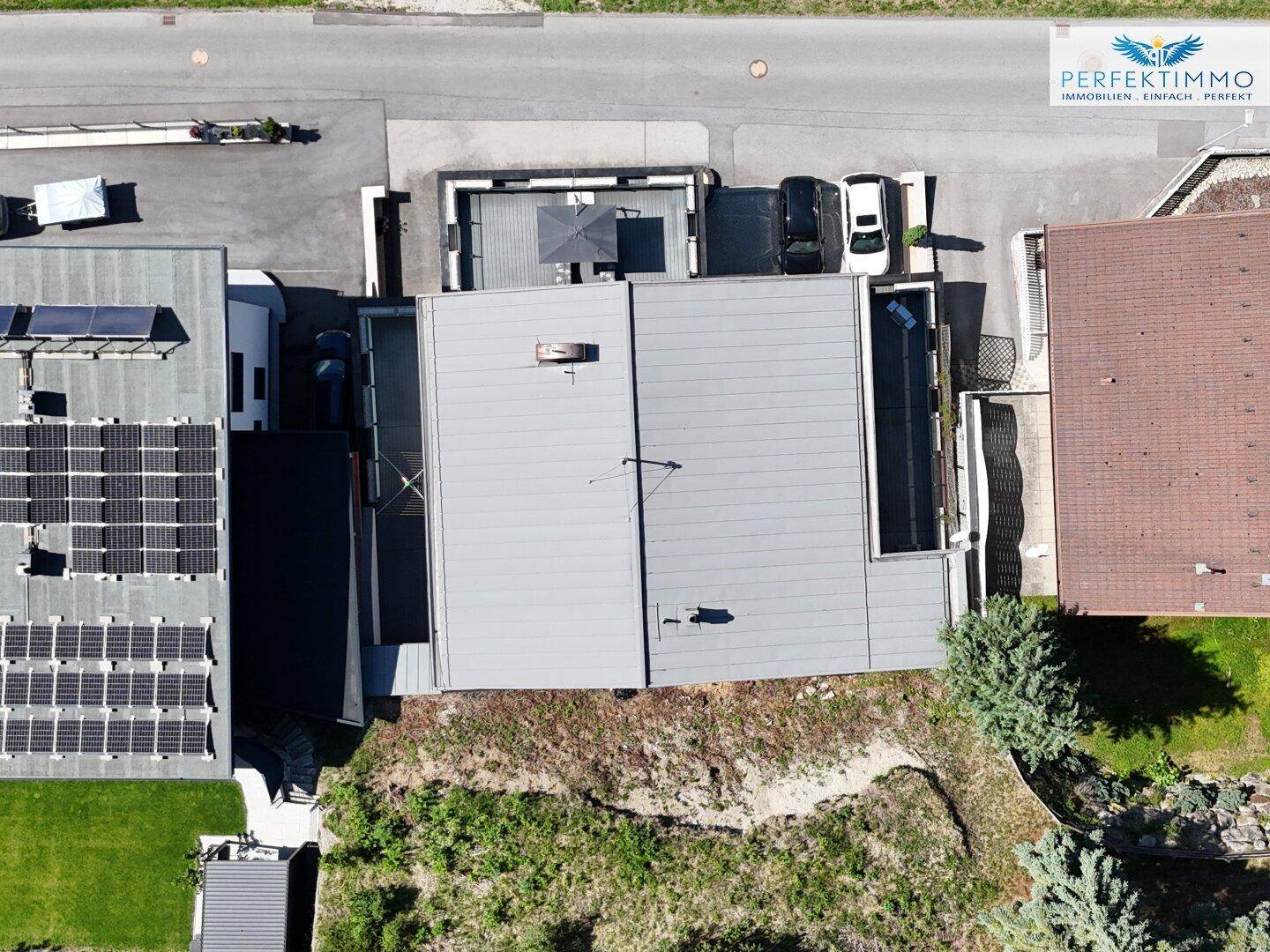 Dachansicht eines Hauses mit Flachdach, Solaranlage und umliegender grüner Natur.