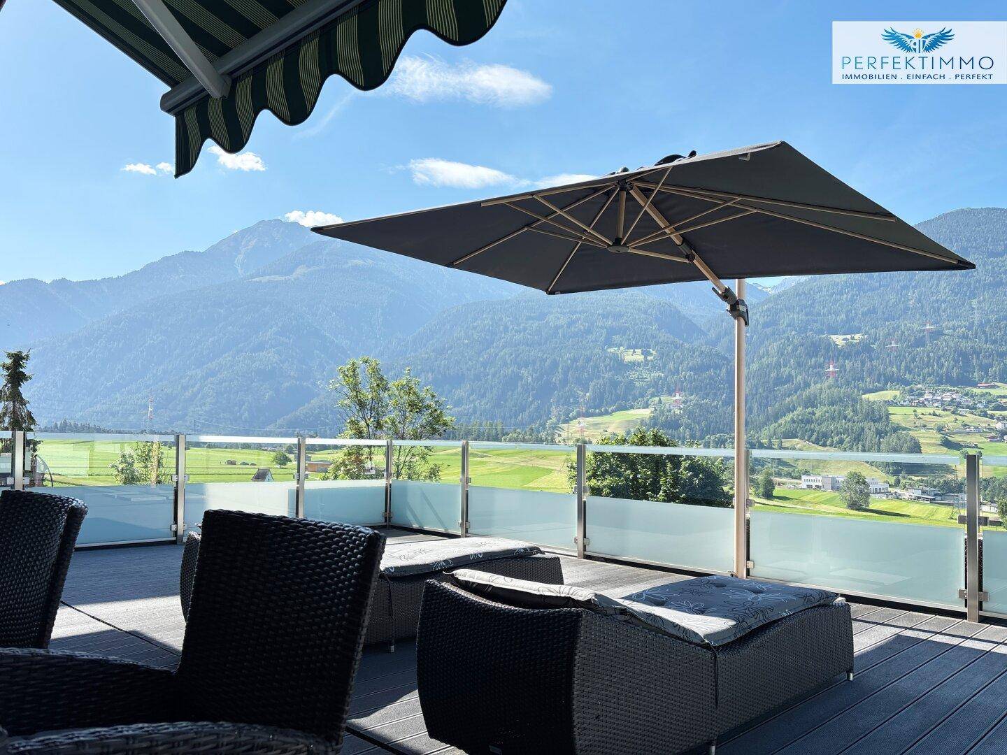 Gemütliche Sitzecke auf der Terrasse mit großem Sonnenschirm und beeindruckendem Bergblick.