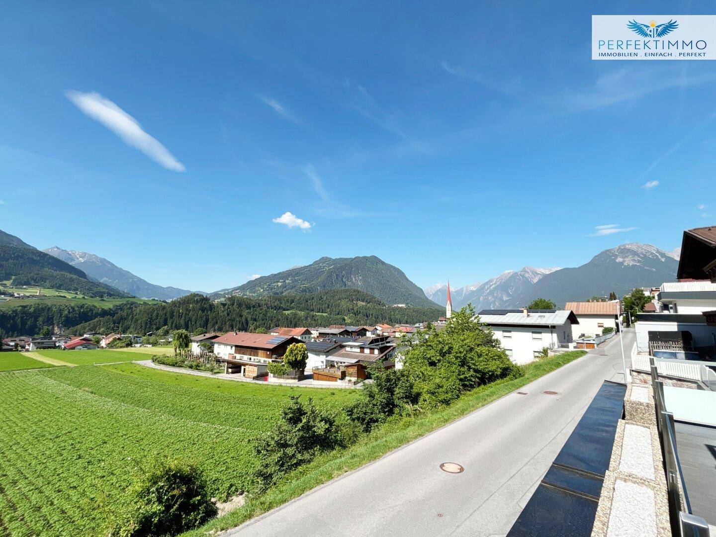 Panoramablick auf die umliegende Bergwelt und ein charmantes Dorf mit grünen Feldern.