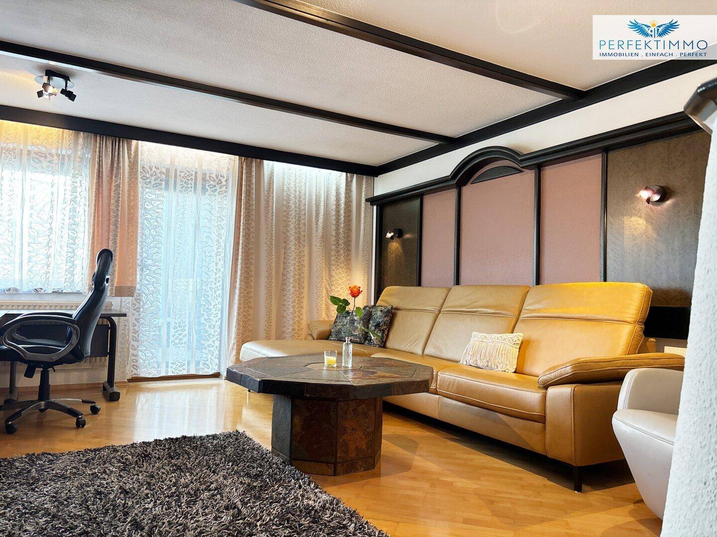 Gemütliches Wohnzimmer mit Ledersofa, Holzboden und Blick auf den Arbeitsbereich.