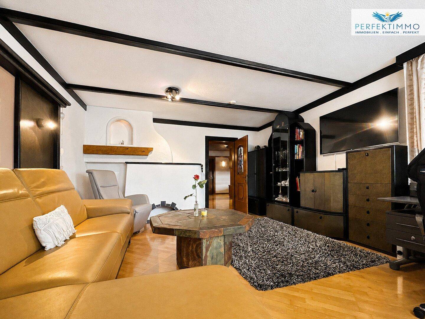 Wohnzimmer mit Kachelofen, Ledersofa und Holzboden, bietet eine warme Atmosphäre.