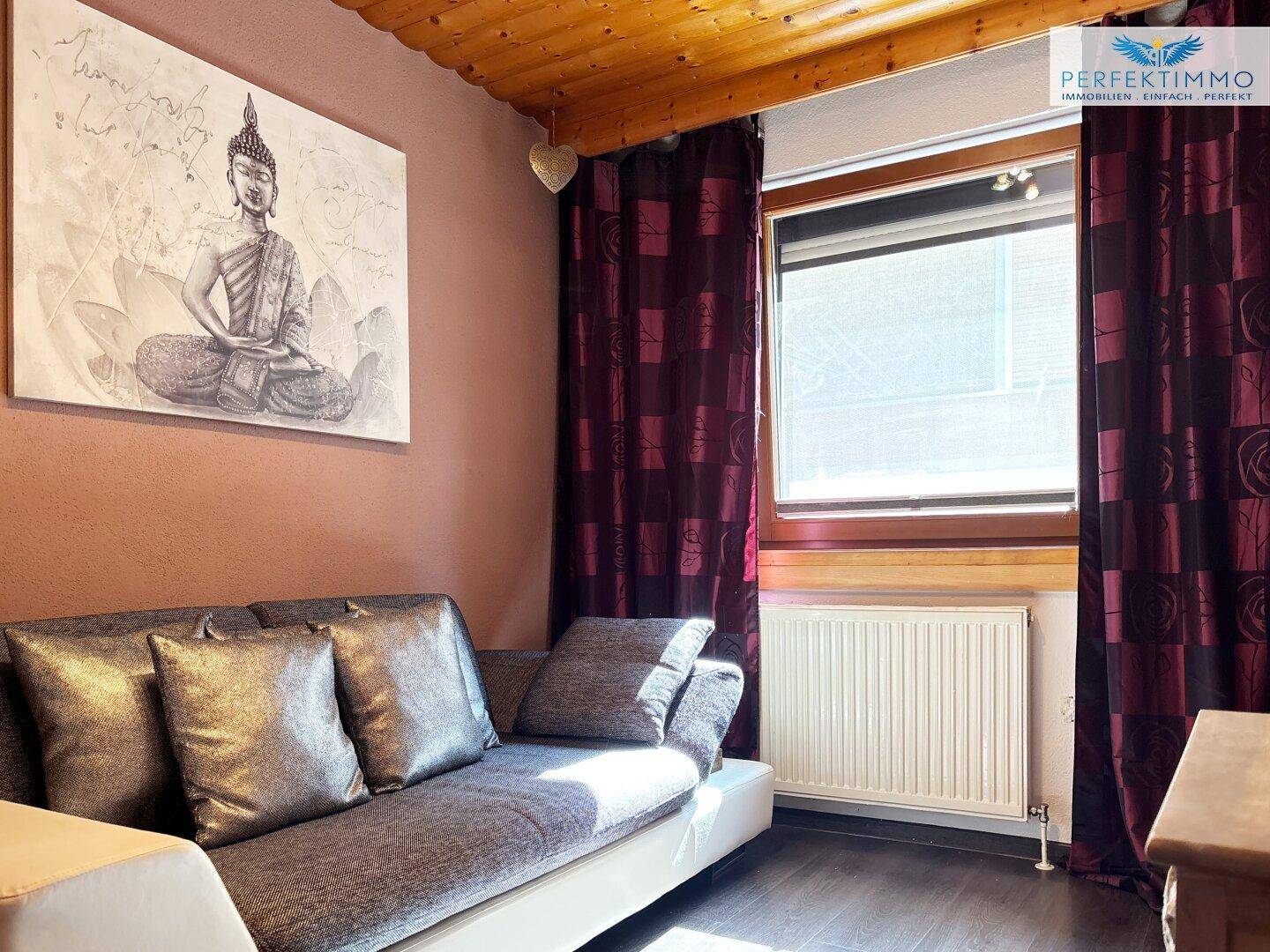 Schlafzimmer mit Sofa, Holzboden und Fenster, das viel Tageslicht hereinlässt.