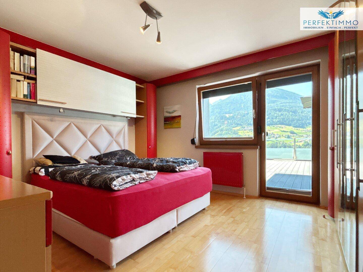 Helles Schlafzimmer mit Doppelbett, Holzboden und Zugang zur Terrasse mit Bergblick.