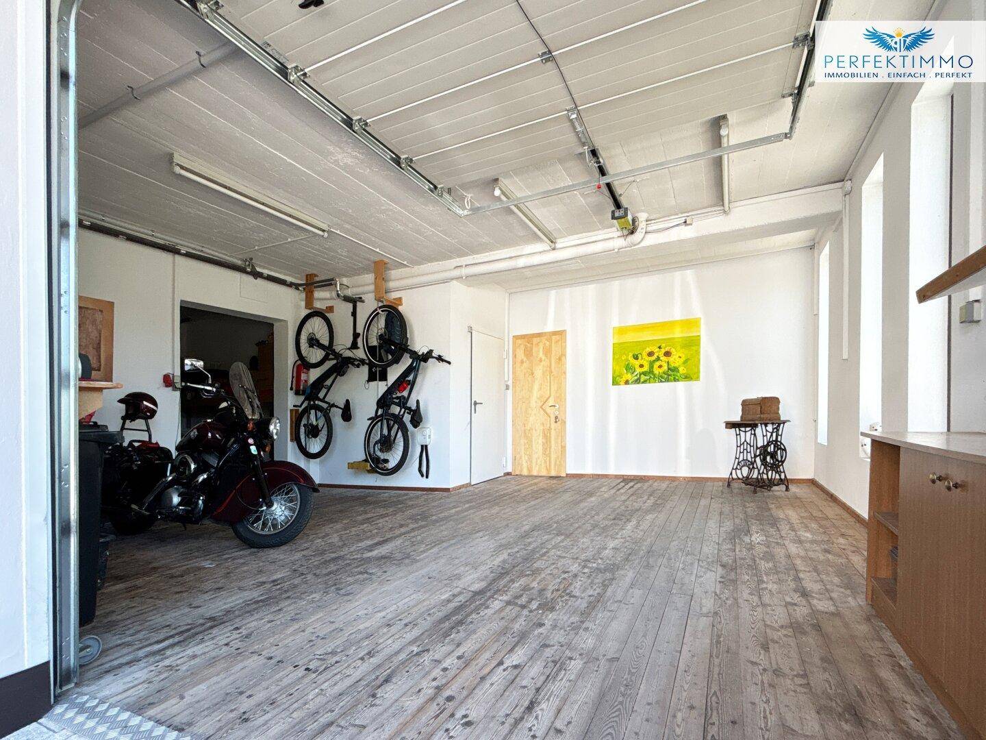 Geräumige Garage mit Holzboden, Fahrrädern an der Wand und einem Motorrad, ideal für Hobbys.