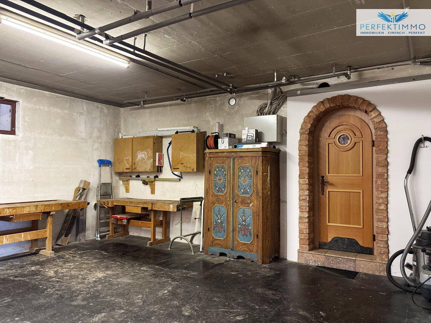 Rustikale Werkstatt im Keller mit Werkbänken, Schränken und einem gemauerten Ziegelbogen als Türrahmen.