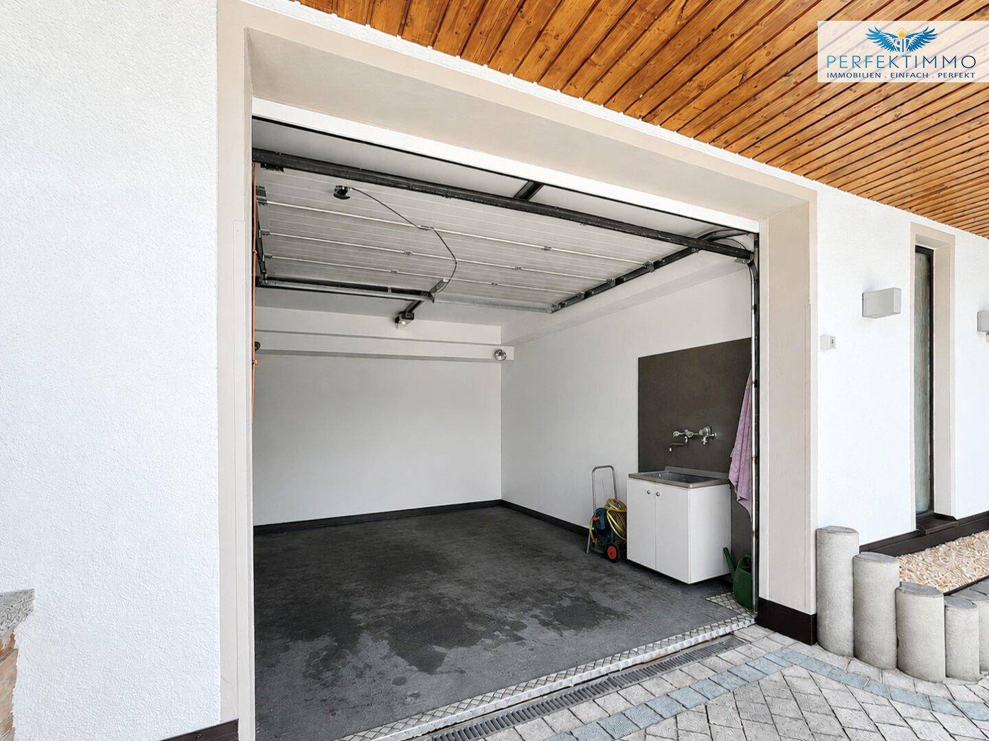 Einzelgarage mit Waschbecken, Betonboden und einer Holzdecke, die eine praktische Nutzung ermöglicht.