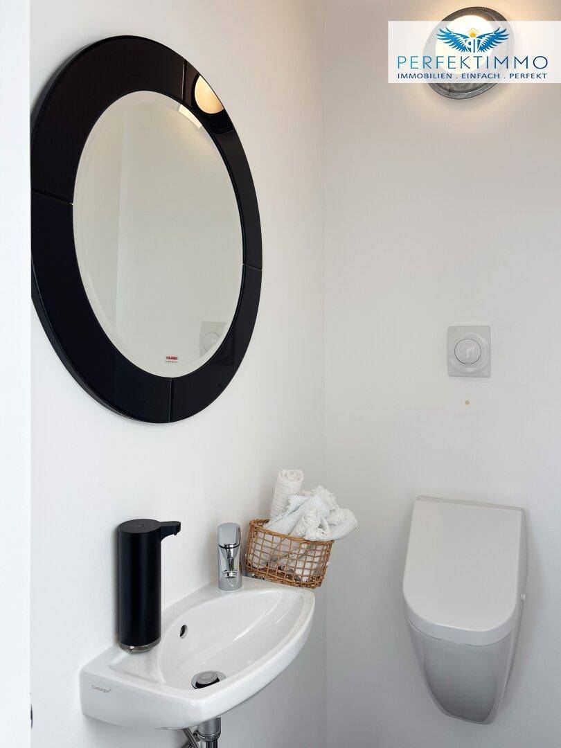 Modernes Gäste-WC mit wandhängender Toilette, kleinem Waschbecken und ovalem Spiegel.