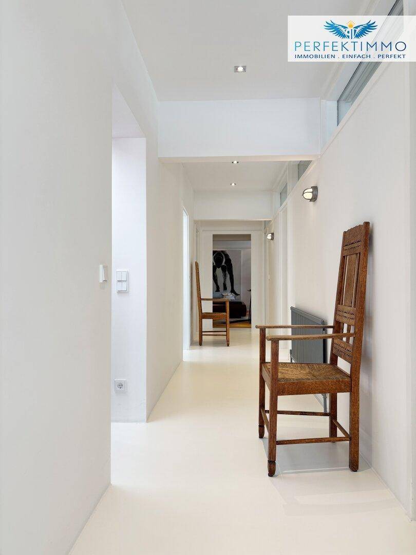 Langer, heller Flur mit weißen Wänden, Holzboden und minimalistischer Dekoration.