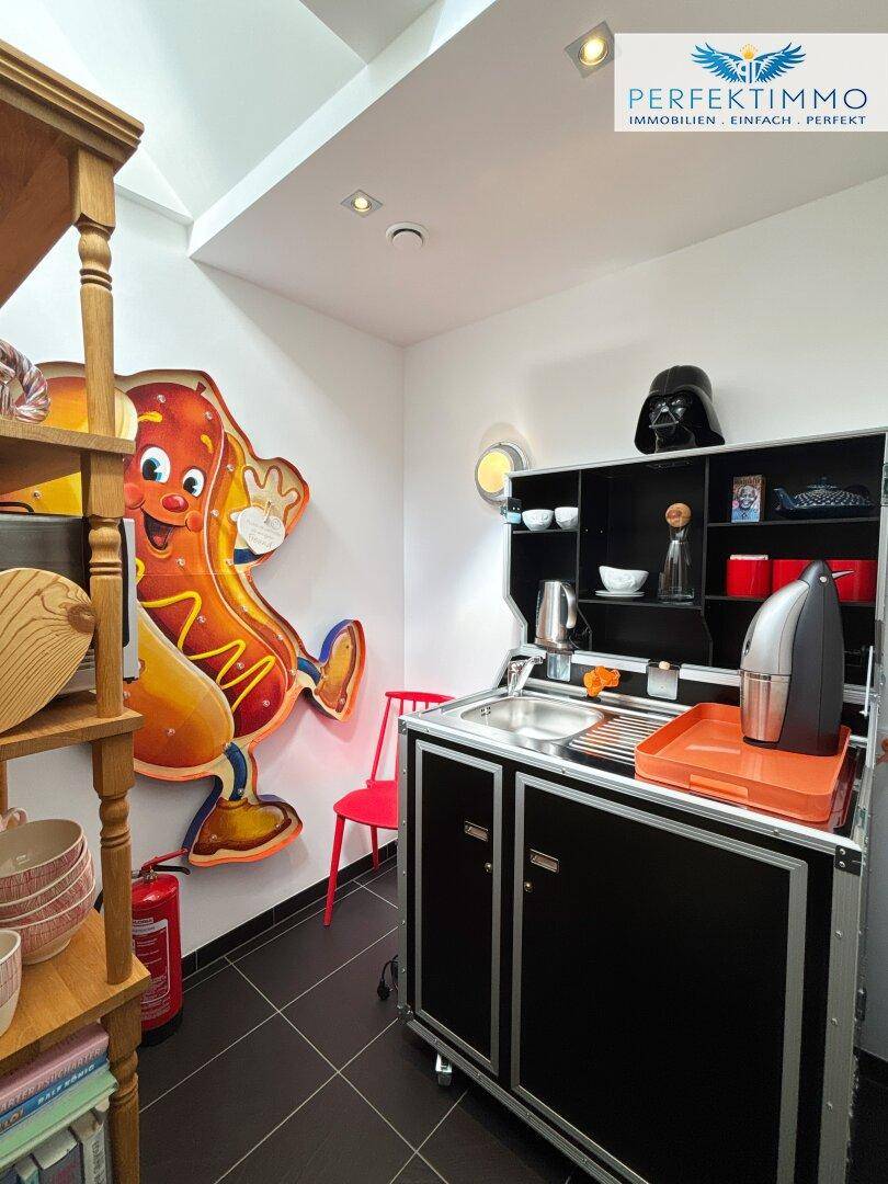 Kompakte Küchenzeile mit Spüle und Stauraum, dekoriert mit einem farbenfrohen Hotdog-Kunstwerk.