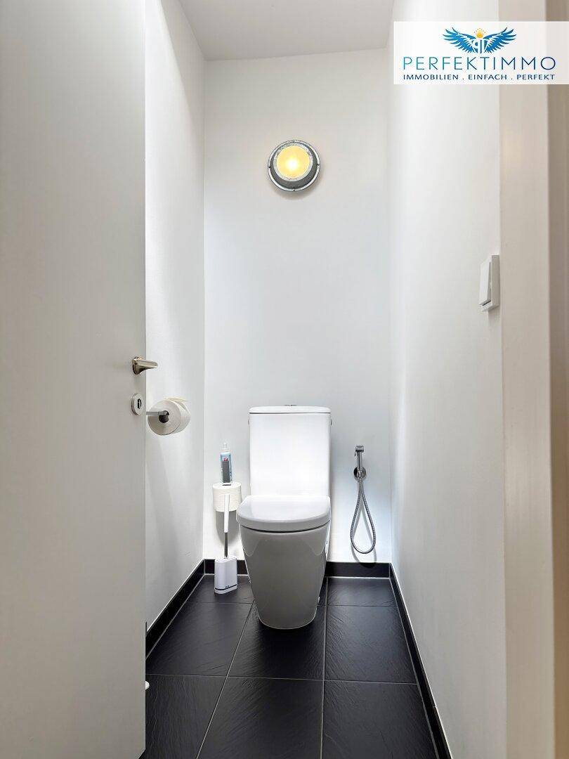 Kleiner Toilettenraum mit dunklen Fliesen und einer wandhängenden Toilette.