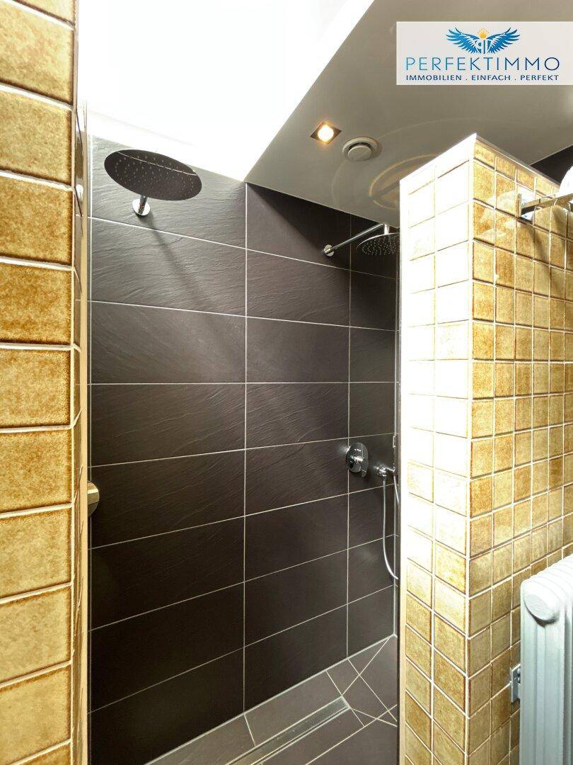 Duschbereich im Badezimmer mit einer Kombination aus beigen und dunklen Fliesen.