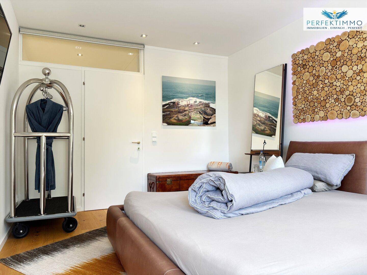Schlafzimmer mit Gepäckwagen, Spiegel und einem modernen Kunstwerk an der Wand.