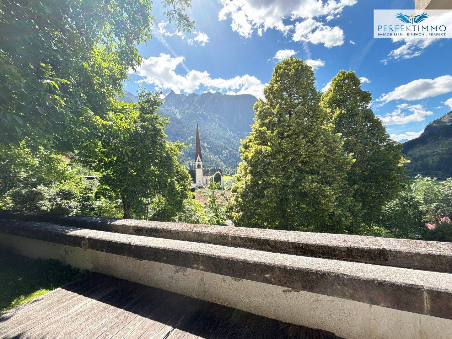 Malerischer Blick auf ein Dorf mit Kirchturm und majestätischen Bergen im Hintergrund.