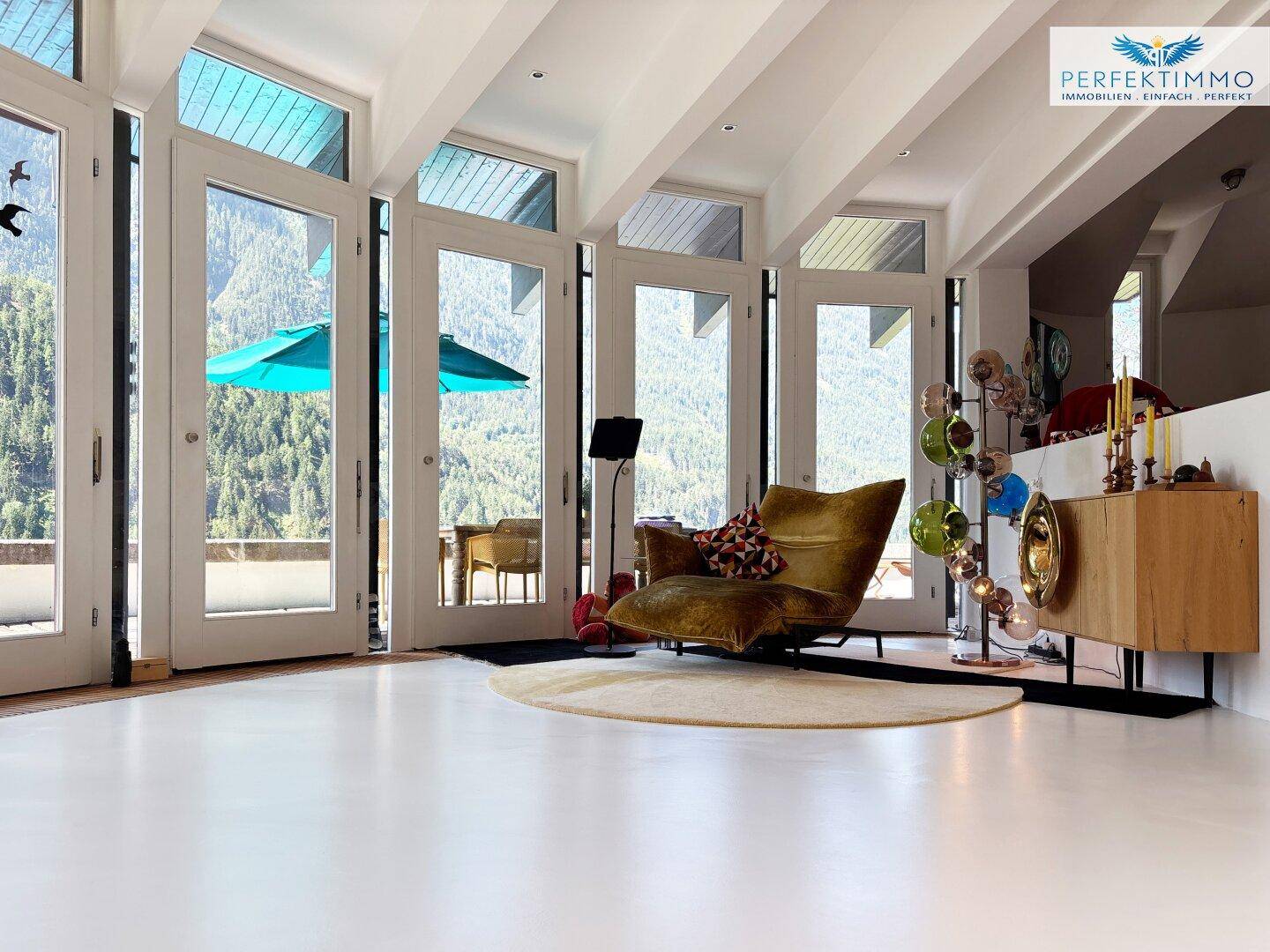 Geräumiges Wohnzimmer mit großen Fenstertüren, die einen atemberaubenden Bergblick freigeben.