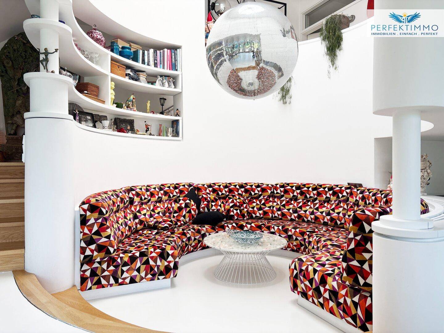 Farbenfroher Wohnbereich mit runder Sitzgruppe, Bücherregal und moderner Dekoration.